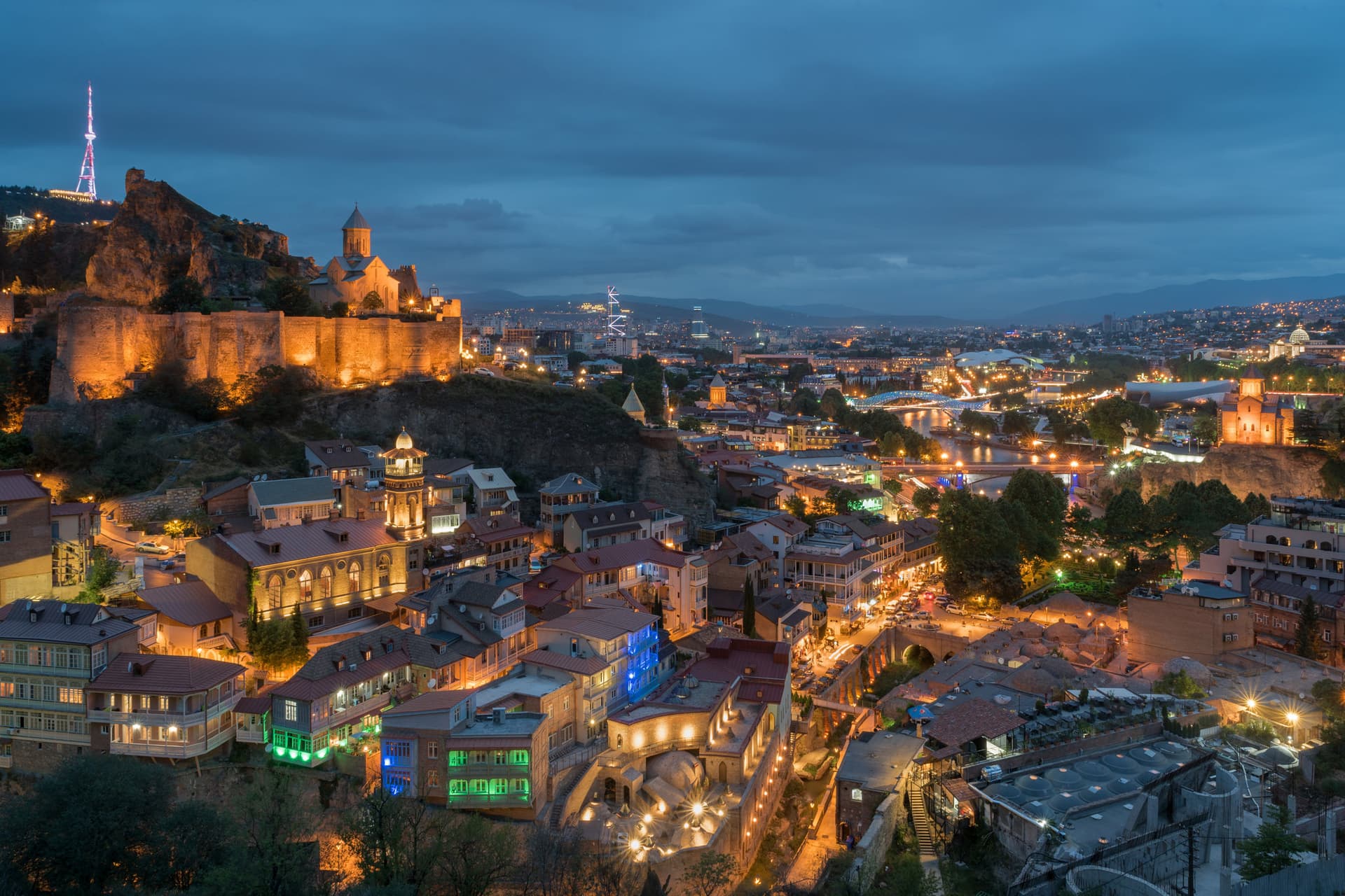 Tbilisi at dusk, Narikala fortress glowing on the hilltop, old town rooftops and the Mtkvari River lit below