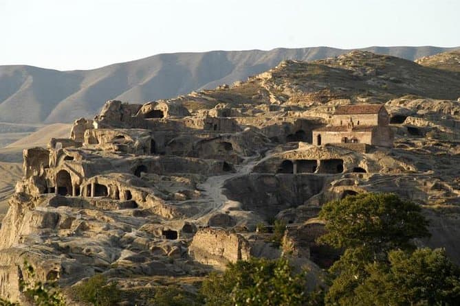 Uplistsikhe ancient cave town carved into golden rock, with a small red-roofed church and rolling hills at dusk
